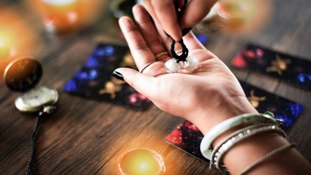 Hand holding pendulum over tarot cards.