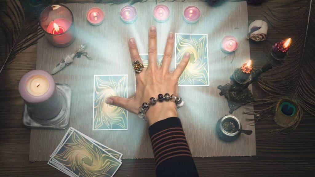 Hand over tarot cards surrounded by candles.