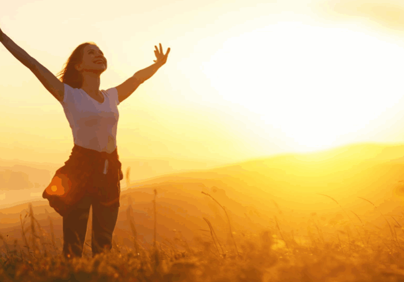 A woman standing in the grass with her arms raised.